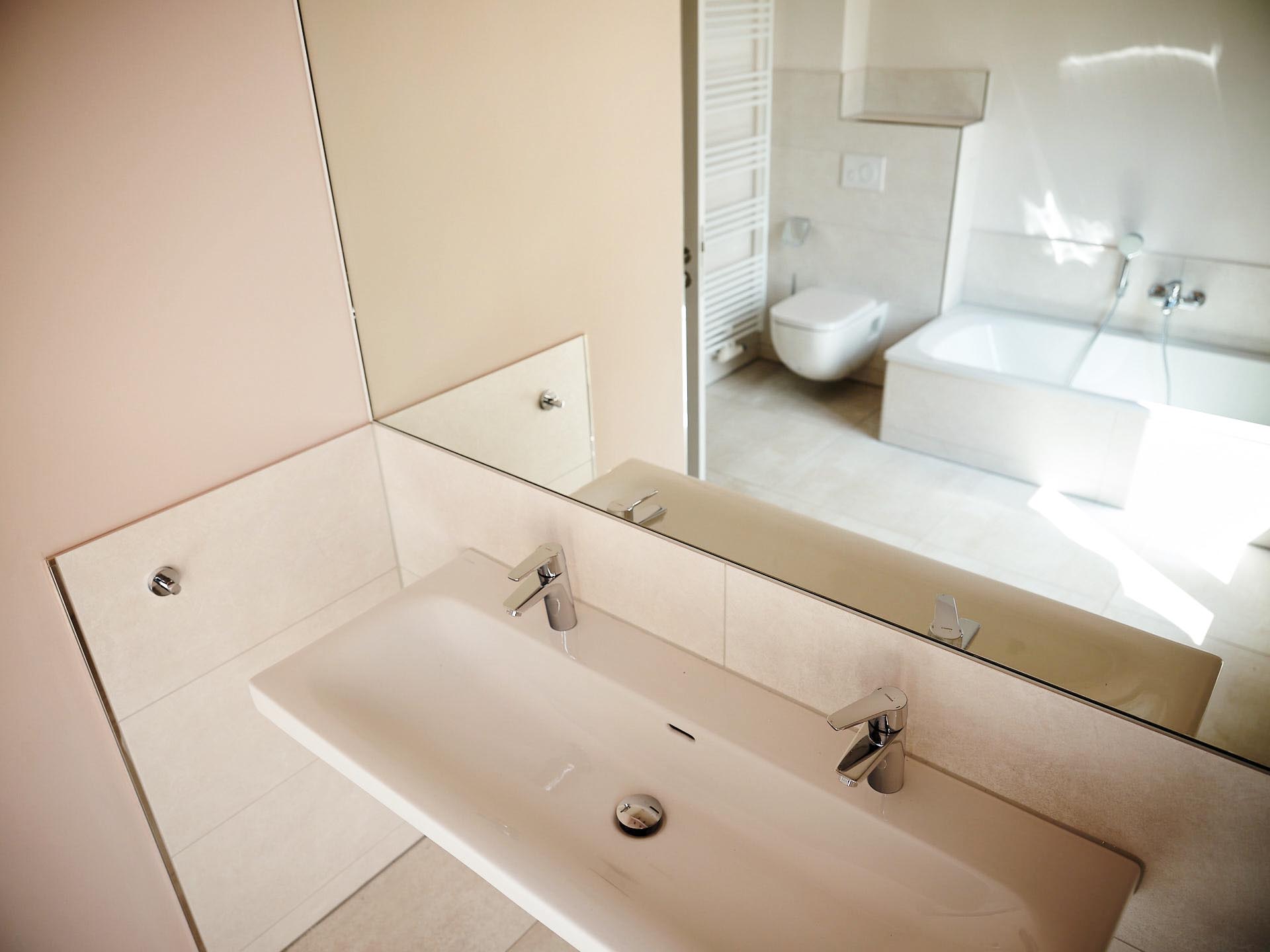 Minimalistisches Badezimmer-Design mit großem Spiegel, Doppelwaschbecken und hochwertiger Armaturen-Ausstattung.